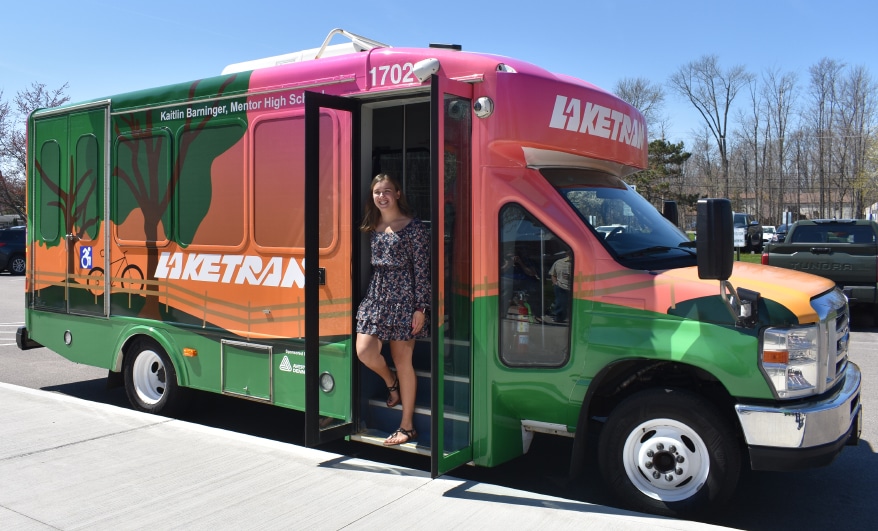 “Contest winner Kaitlin Barninger stands aboard the Laketran bus wrapped in her design.” PHOTO CREDIT: Images © 2023 Avery Dennison Corporation
