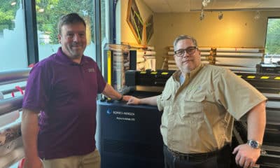 Eric Hilden, General Manager at GAM Graphics and Marketing (at left) and Nathaniel Grant, President, GAM Graphics and Marketing stand with their newly installed Konica Minolta AccurioWide 250 hybrid UV LED wide format inkjet printer. This was the first installation of the new device since its launch in April 2023.