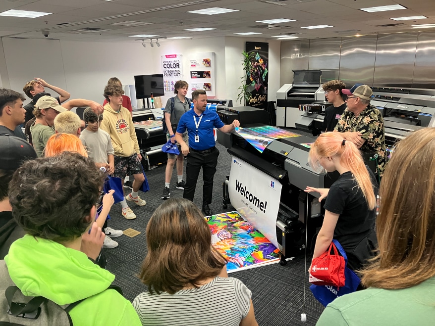 Roland DGA’s sales manager for the Education market, Garrett Smawley (center in photo) demonstrates some of the impressive capabilities of the company’s advanced wide-format inkjet printers for visiting Laguna Beach High School students. The students, who are taking visual arts classes, visited Roland DGA’s Irvine, California headquarters as part of National Manufacturing Day and ISA Sign Manufacturing Day.